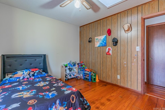 bedroom with wooden walls, a ceiling fan, and wood finished floors