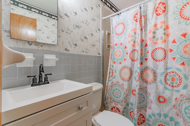 bathroom with wallpapered walls, a wainscoted wall, a shower with curtain, tile walls, and a sink