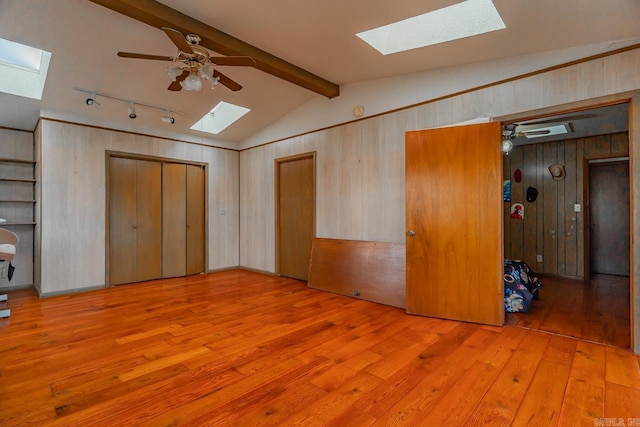 unfurnished bedroom with ceiling fan, wood walls, vaulted ceiling with beams, and hardwood / wood-style flooring