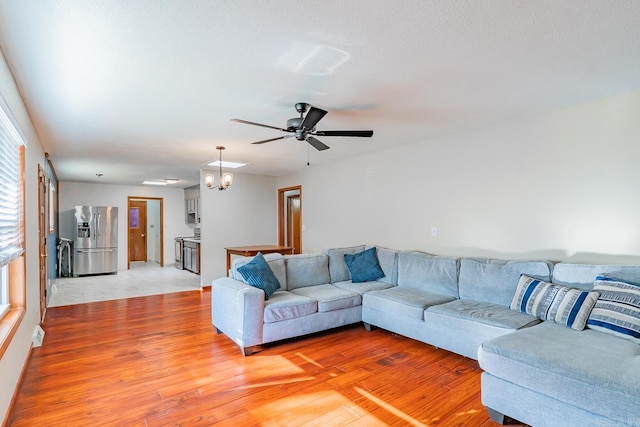 living area featuring ceiling fan with notable chandelier and light wood-style floors