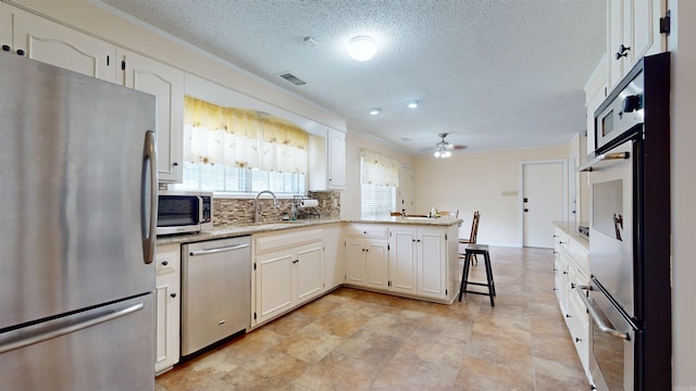 kitchen featuring a peninsula, white cabinets, appliances with stainless steel finishes, and a sink