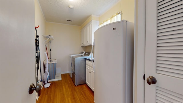 laundry area featuring light wood-type flooring, visible vents, washer and clothes dryer, a textured ceiling, and cabinet space