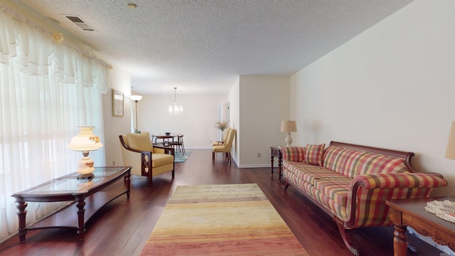 living room with visible vents, baseboards, an inviting chandelier, wood finished floors, and a textured ceiling