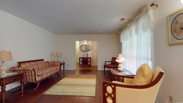 living room featuring visible vents, a textured ceiling, baseboards, and wood finished floors