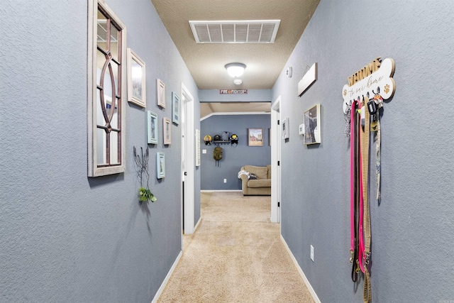 hallway with visible vents, carpet flooring, baseboards, and a textured wall