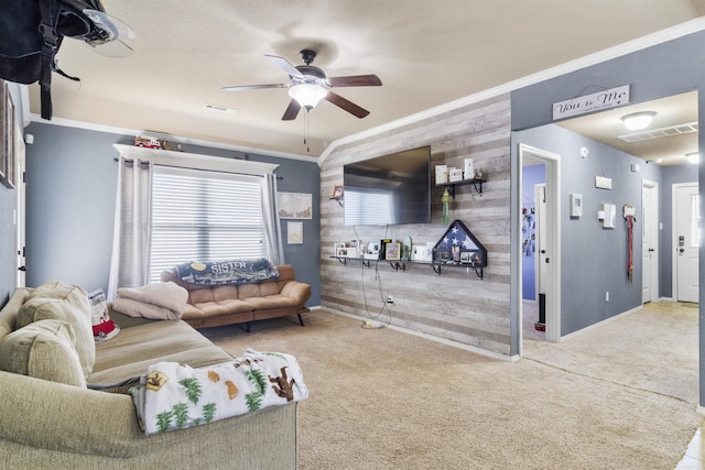 carpeted living room with visible vents, wooden walls, ornamental molding, and a ceiling fan