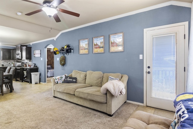 living room with baseboards, vaulted ceiling, ornamental molding, arched walkways, and a ceiling fan