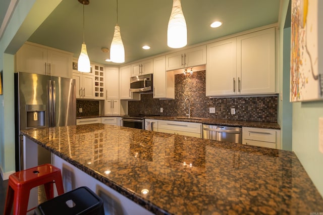 kitchen with a sink, dark stone countertops, tasteful backsplash, appliances with stainless steel finishes, and a breakfast bar area