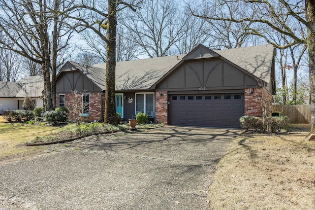 english style home with brick siding, an attached garage, driveway, and fence