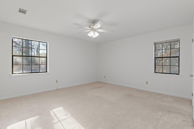 empty room with light colored carpet, a ceiling fan, visible vents, and baseboards