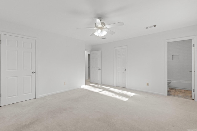 unfurnished bedroom featuring visible vents, baseboards, ceiling fan, ensuite bathroom, and light colored carpet