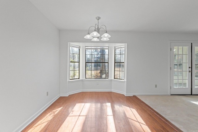 unfurnished dining area with baseboards, an inviting chandelier, and hardwood / wood-style flooring