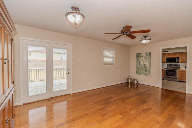 unfurnished living room with visible vents, light wood-style flooring, a textured ceiling, baseboards, and ceiling fan