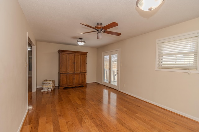 spare room with light wood-style flooring, a ceiling fan, baseboards, and a textured ceiling