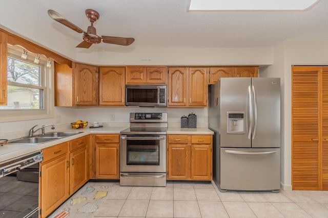 kitchen with a sink, ceiling fan, light countertops, stainless steel appliances, and brown cabinets