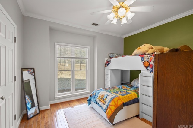 bedroom with light wood-type flooring, visible vents, a ceiling fan, crown molding, and baseboards