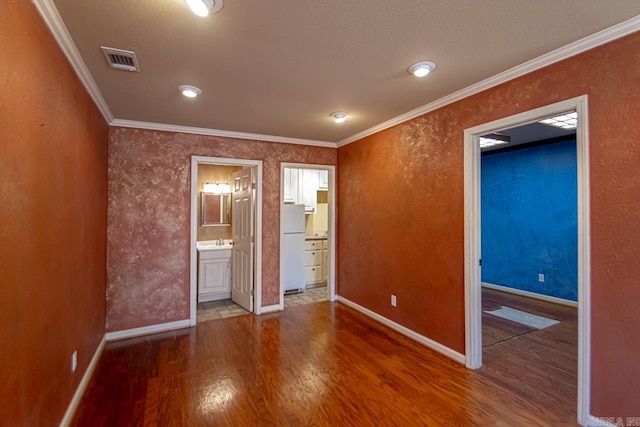 unfurnished room featuring wood finished floors, visible vents, baseboards, a sink, and crown molding