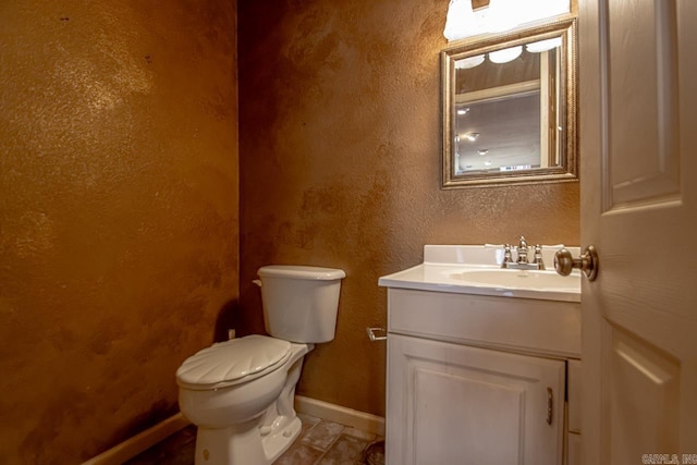 half bathroom with toilet, vanity, baseboards, and a textured wall