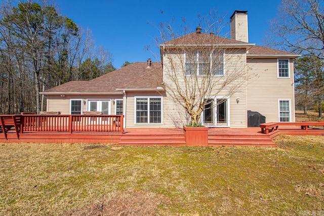 rear view of property with a yard, a wooden deck, a chimney, and a shingled roof