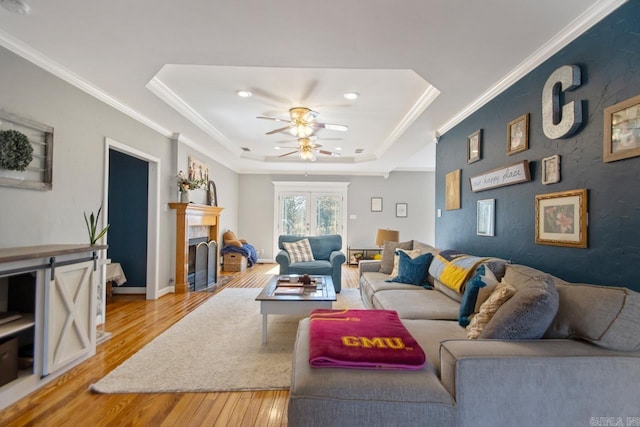 living room with light wood-style flooring, a ceiling fan, a fireplace, crown molding, and a raised ceiling