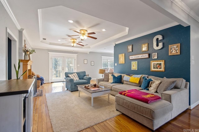 living room with a raised ceiling, light wood-style flooring, a ceiling fan, and crown molding