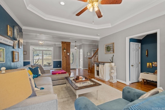 living room with wood finished floors, a tray ceiling, ornamental molding, stairs, and ceiling fan