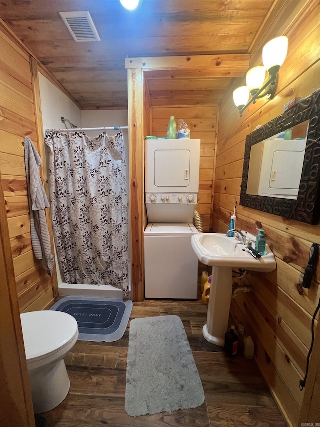 bathroom featuring wooden walls, wood finished floors, visible vents, stacked washer / drying machine, and wooden ceiling