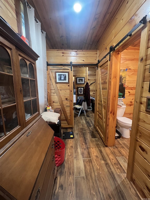 interior space with a barn door, wooden walls, dark wood-style floors, and wooden ceiling