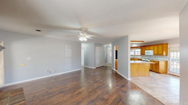 unfurnished living room with plenty of natural light, light wood-style flooring, baseboards, and ceiling fan