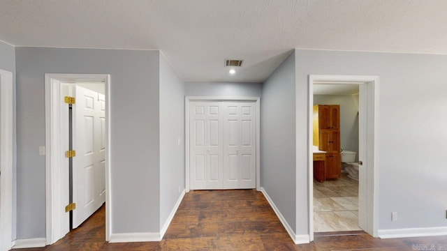 hallway with baseboards, visible vents, dark wood-style flooring, and a textured ceiling