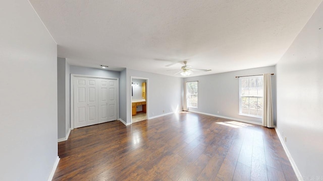 empty room featuring a textured ceiling, baseboards, a ceiling fan, and dark wood-style flooring