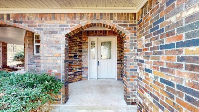 view of exterior entry with brick siding and a porch