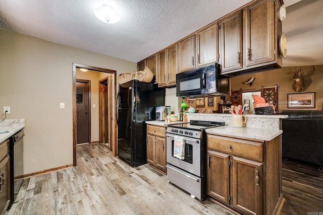 kitchen featuring baseboards, a peninsula, black appliances, a textured ceiling, and light wood-type flooring