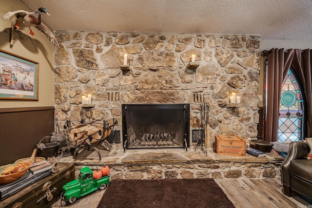 room details featuring a stone fireplace, a textured ceiling, wood finished floors, and wainscoting