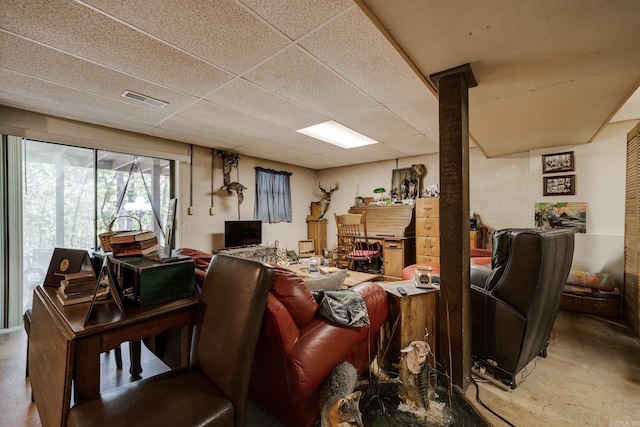 living area with concrete block wall, a paneled ceiling, visible vents, and concrete floors