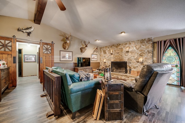 living room featuring lofted ceiling with beams, a barn door, wood finished floors, and a ceiling fan