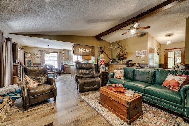 living area featuring light wood-style floors, ceiling fan, vaulted ceiling with beams, and a textured ceiling