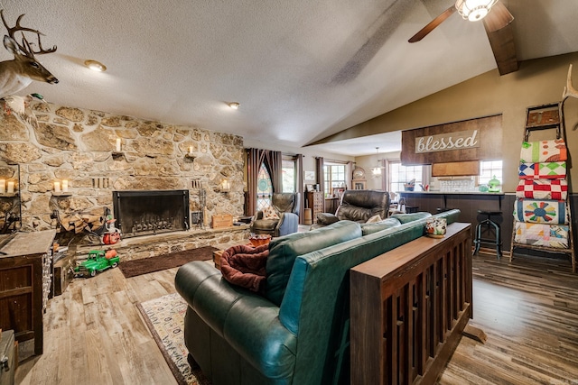 living room with wood finished floors, a fireplace, ceiling fan, vaulted ceiling, and a textured ceiling