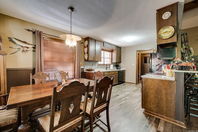 dining room with a notable chandelier, wainscoting, light wood-type flooring, and a textured ceiling