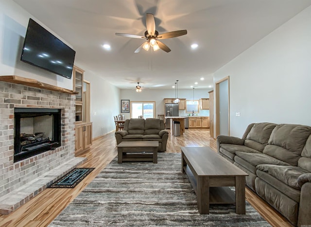 living area with recessed lighting, a brick fireplace, a ceiling fan, and light wood finished floors