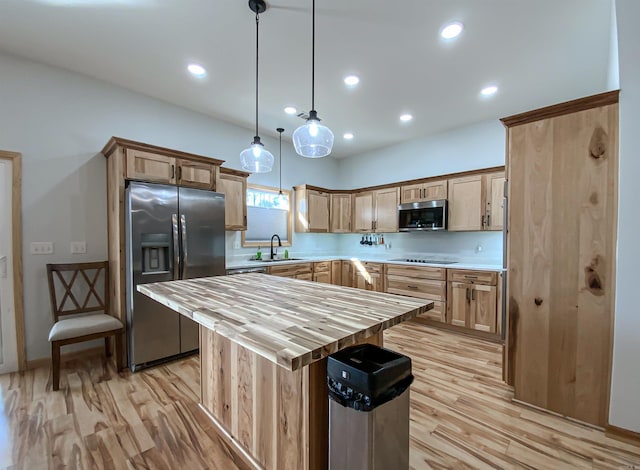 kitchen featuring wooden counters, light wood-style flooring, a sink, hanging light fixtures, and stainless steel appliances