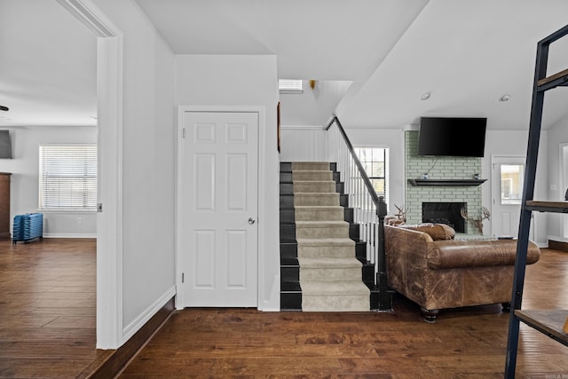 staircase featuring baseboards, a healthy amount of sunlight, hardwood / wood-style floors, and a fireplace