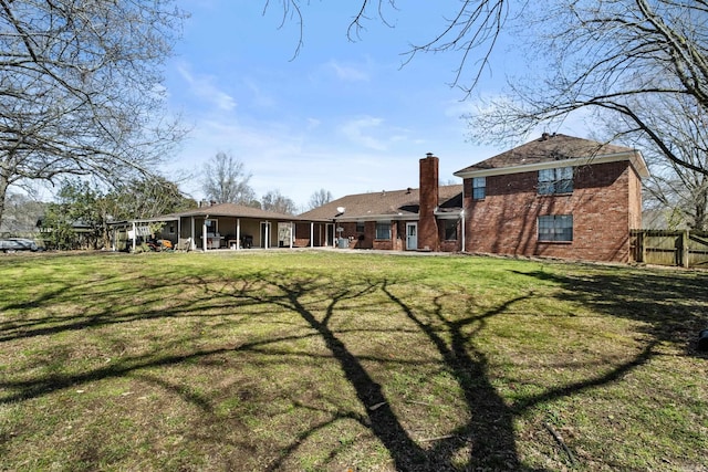 back of house with brick siding, a chimney, a yard, and fence