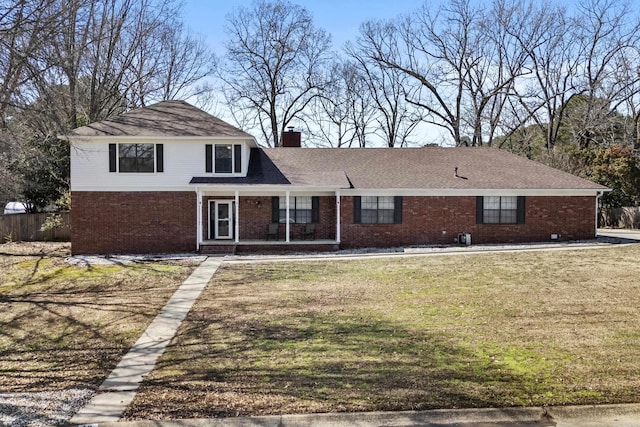 traditional-style home with a porch, brick siding, a chimney, and a front lawn