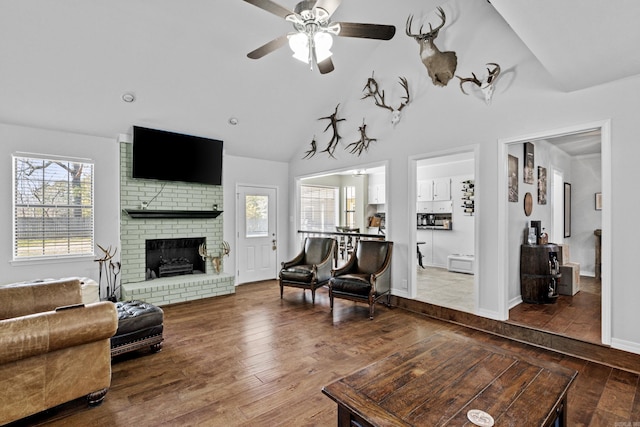 living area featuring a brick fireplace, high vaulted ceiling, a ceiling fan, and wood-type flooring