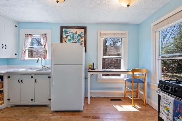 kitchen featuring gas range, freestanding refrigerator, light wood-style floors, white cabinetry, and a sink