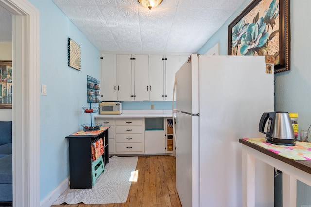 kitchen featuring baseboards, light countertops, light wood-style flooring, white cabinets, and white appliances