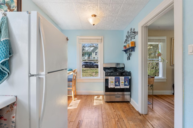 kitchen with gas stove, baseboards, freestanding refrigerator, and light wood-style floors