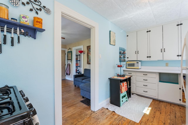 kitchen with white microwave, baseboards, light wood-style flooring, white cabinets, and gas range oven