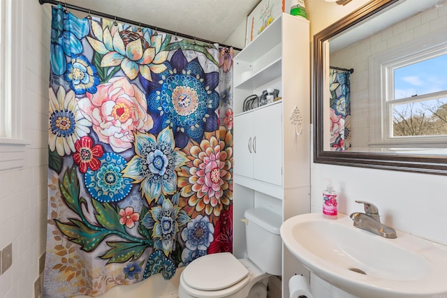 full bath featuring a shower with shower curtain, toilet, and a sink